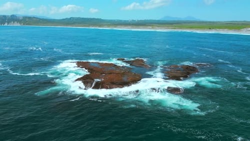 Aerial view of ocean waves crashing into rocks. Clip. Flying above turquoise water and giant boulder