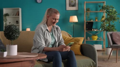 Smiling Woman Sitting on Sofa Using Phone