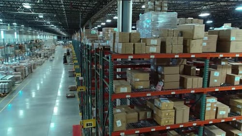 A rotating drone shot around the end of a tall warehouse shelving row, revealing multiple aisles,