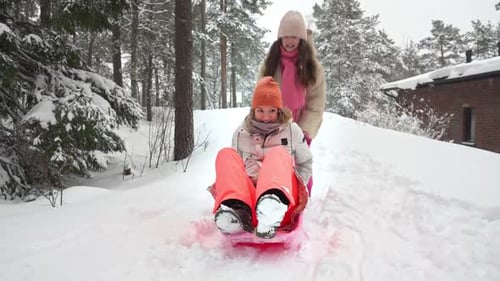 Mother and Daughter Laughing While Sledding in Snowy Forest