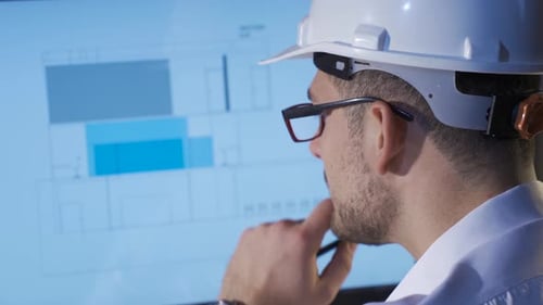 Engineer examines architectural drawing on computer in his office.