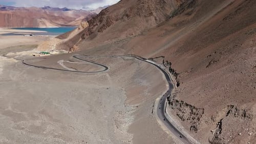 Group of Motorcyclists Riding on Curved Asphalt Road in Tibetan Mountain Desert