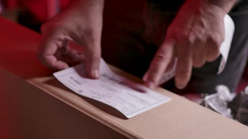 The hands of a male warehouse worker putting an adhesive label with the printed shipping information