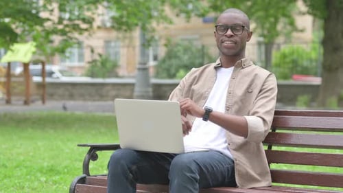 Young African Man Smiling with Laptop in Park