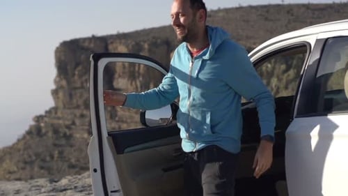 Young man steps from car to admire majestic canyon vista in slow motion