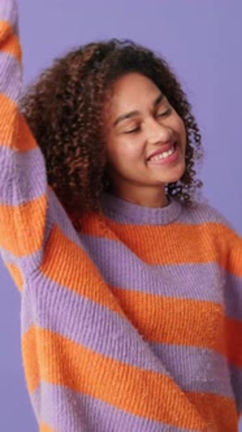Happy young woman dancing on lilac background in studio