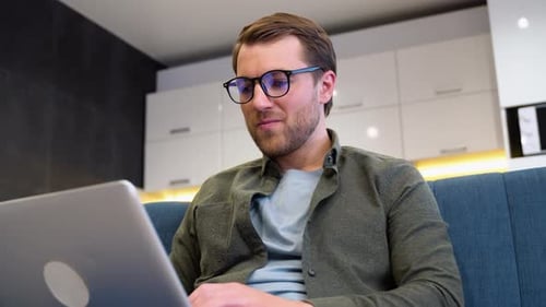 Smiling Man Uses Laptop on Couch Indoors