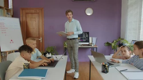 Young Teacher Explaining Test Tasks to Group of Kids at IT Class