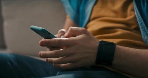 Young Man Uses Phone Closeup of Hands Scrolling Finger Across Screen Writing Messages Browsing