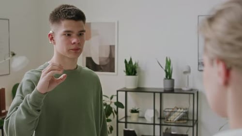 Jeune homme avec un implant cochléaire récitant l'alphabet en langue des signes à l'enseignant