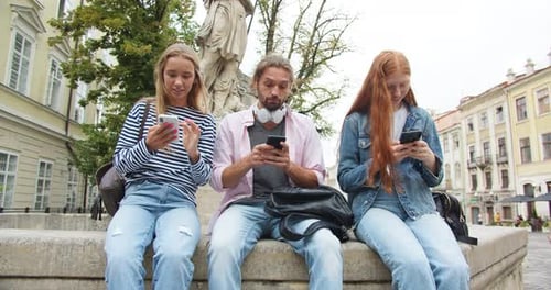 Female and Male Students Sitting on Bench and Using Gadgets for Communication Young Man and Women
