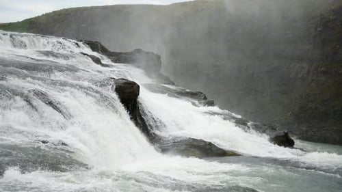 Gorgeous static scenic shot of majestic waterfall careens over river rocks forming white water rapid