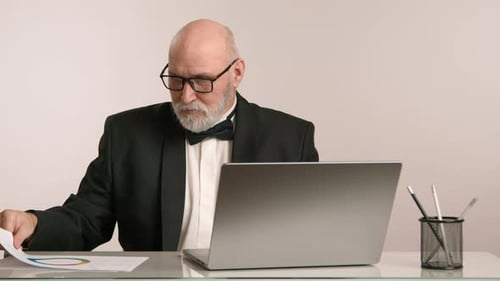 Senior Businessman Reviewing Documents Laptop on Desk