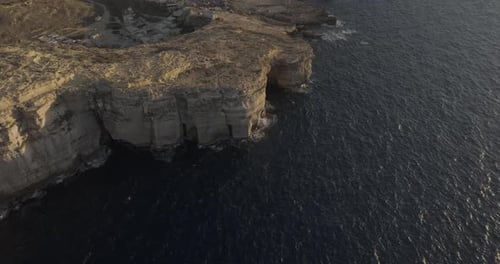 Aerial view of rugged Gozo cliffs and Dwejra Bay at sunset, Munxar, Malta.