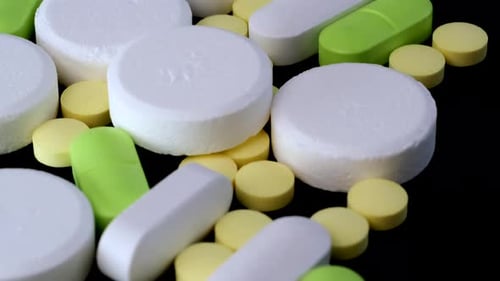 Heap different colors pills lying on black table tracking shot, close-up. Medical care and health.