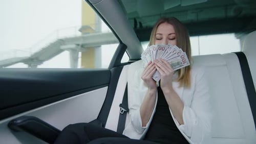 Businesswoman Holding a Fan Made of Dollar Bills and Sniffing It