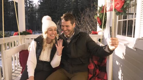 Couple video calling family to announce engagement on porch swing in Canada