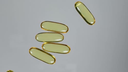 Una cápsula de aceite de pescado se enrolla para formar una pila de cápsulas con vitamina E o aceite de pescado sobre la mesa.