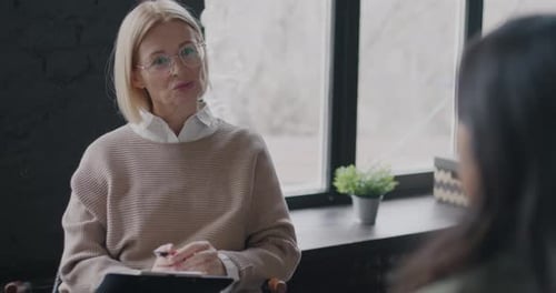 Mature Lady Psychologist Talking to Female Client Giving Advice and Support Indoors in Light Office