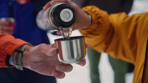Person pouring hot tea from thermos in winter