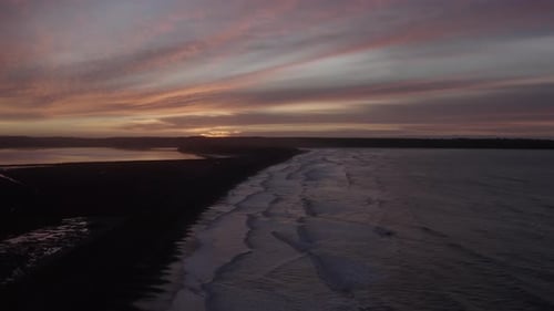 Predawn sunrise colour on sea coast, waves gently roll onto dark beach