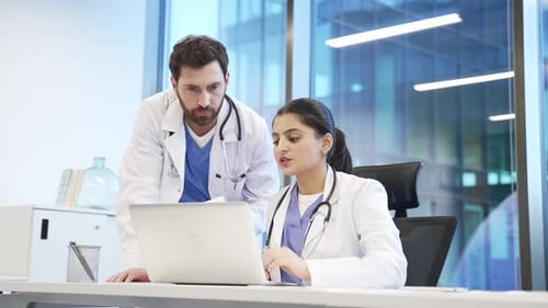 A team of two doctors having a professional discussion in office with a laptop. Female and male