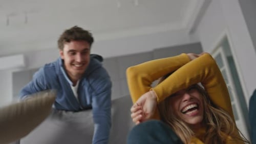 Playful Couple Pillow Fight on Sofa at Home