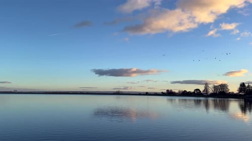 Blaues Seewasser mit goldenem Sonnenuntergangshimmel, verträumte Wolken. Perfekter Winterabend. Pastellblauer Farbton mir