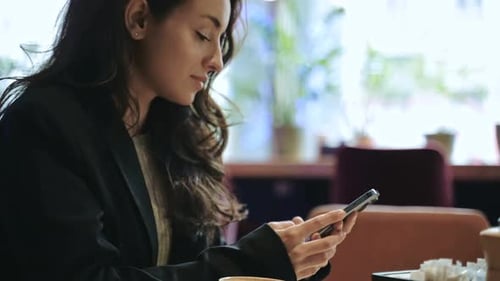 Young Charming Woman Using Smartphone While Sitting Alone in Coffee Shop