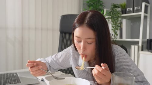 Asian young businesswoman eating noodles while working in the office.