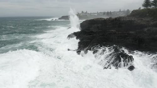 Fly around shot of angry ocean exploding onto the rocky shore line. Stormy weather.