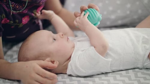 Infant Plays with Toy Beside Adult on Bed