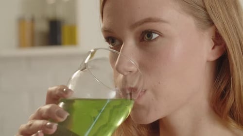 Young Woman Drinking Green Juice Detox Cocktail in the Kitchen at Home