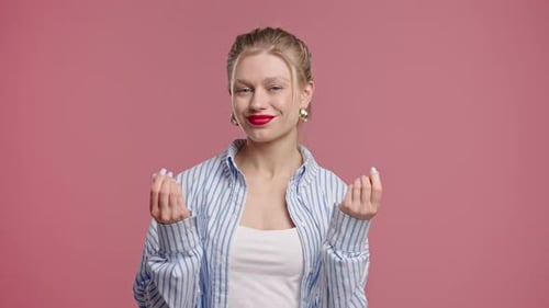 Smiling Woman Making Money Gesture With Playful Mischievous Look On Pink Studio