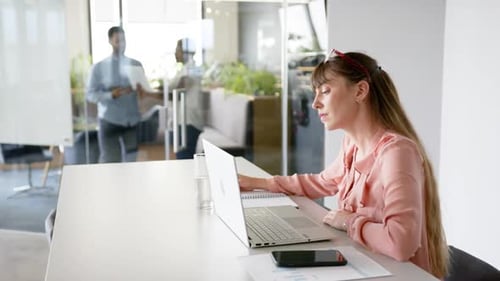 Working in office, woman using laptop and writing in notepad at desk, copy space