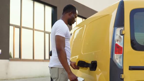 African American Man Charging Cargo Electric Car Near Warehouse Green Energy Eco Friendly Fuel