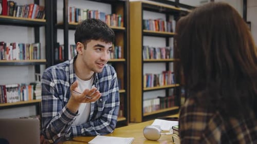 Young Man Engages in Conversation with a Woman in a Cozy Library Setting During the Afternoon