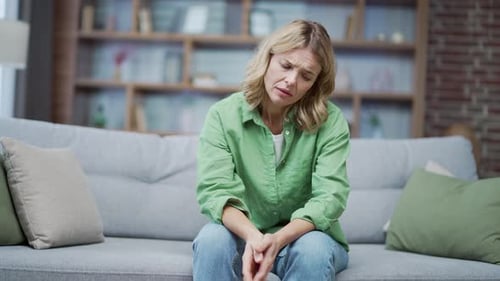Die reife blonde Frau hat schlechte Laune, wenn sie zu Hause auf dem Sofa im Wohnzimmer sitzt. Verärgerte Frau