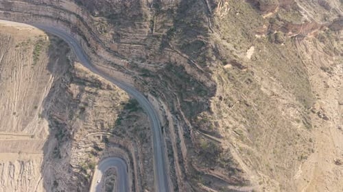 Aerial View of a Winding Mountain Road with Hairpin Turns and Cars Traveling Through Steep Rocky