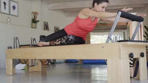 Fit senior caucasian woman stretching on reformer in pilates studio, unaltered, in slow motion