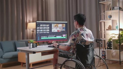 Back View Of Asian Man In Wheelchair Is Using A Desktop Next To The Camera Editing The Video At Home