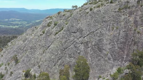 Aerial approaches unique rock outcrop to reveal climbers on summit
