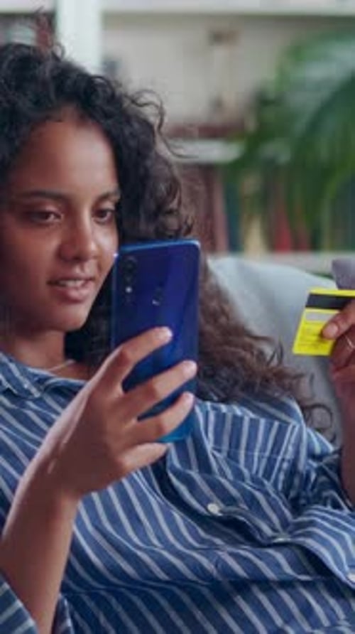 Woman Using Phone and Credit Card Indoors