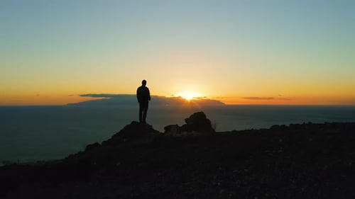 Person Standing on Top of Rock with Epic Mountain Viewpoint Colorful Sunset and Endless Ocean