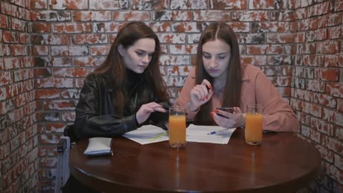 Two Beautiful Girls are Sitting in a Cafe and Talking with Phones