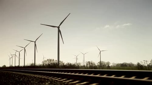 Panoramablick, rotierende Windräder neben Bahngleisen, Sonnenuntergang, blauer Himmel