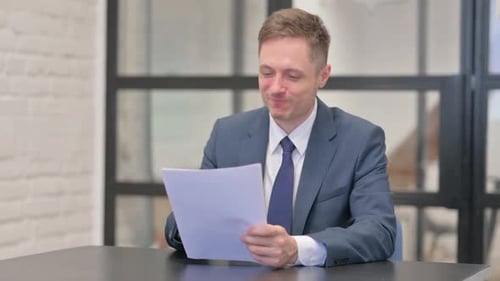 Man in Suit Reviews Documents at Office Desk