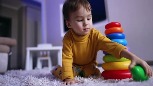 Serious baby boy sits on the floor playing with pyramid.