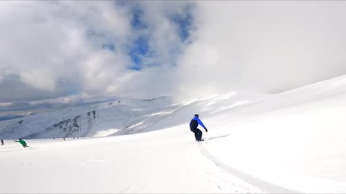 Ich folge einem Sportler beim Snowboarden in den Bergen. Atemberaubende Landschaft unter bewölktem Himmel im Hintergrund.