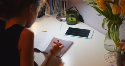 Mädchen sitzt am Schreibtisch und blättert Seiten des Notizbuchs durch, während sie einen Stift hält